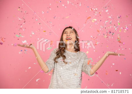 Portrait of a cheerful beautiful Asian womanl wearing dress standing standing under confetti rain and celebrating isolated over pink background Portrait of a cheerful beautiful Asian womanl wearing dress standing standing under confetti rain and celebrating isolated over pink background 81718571