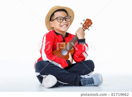 Lovey cutout portrait of young Asian boy wearing brown hat, glasses, red shirt, and long black pants happily sitting with smile while enjoy performing as musician by playing small guitar Lovey cutout portrait of young Asian boy wearing brown hat, glasses, red shirt, and long black pants happily sitting with smile while enjoy performing as musician by playing small guitar 81719662