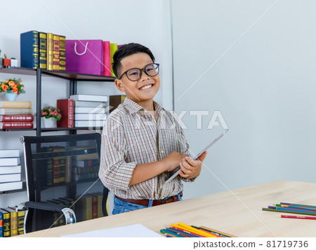 Young Asian boy on black shirt happily resting on chair of white working desk of laptop in home office with hands behind head, smile, and eye close as satisfying and relieve on job success 81719736