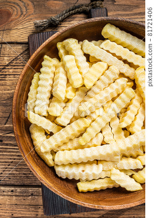 Cold Frozen Crinkle oven French fries potatoes sticks in a wooden plate. Wooden background. Top view Cold Frozen Crinkle oven French fries potatoes sticks in a wooden plate. Wooden background. Top view 81721406