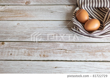 Brown chicken eggs lay on the wooden floor with brown fabric. 81722729