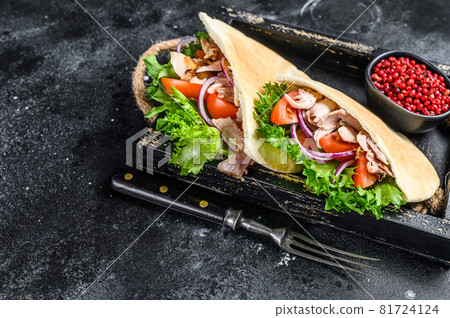 Doner kebab with grilled chicken meat and vegetables in pita bread on a wooden tray. Black background. Top view. Copy space Doner kebab with grilled chicken meat and vegetables in pita bread on a wooden tray. Black background. Top view. Copy space 81724124