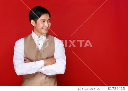 Young attractive Asian man soon to be groom wearing white shirt and beige vest against red background. Concept for pre wedding photography 81724415