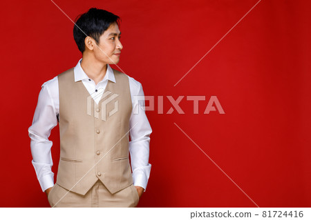 Young attractive Asian man soon to be groom wearing white shirt and beige vest against red background. Concept for pre wedding photography 81724416