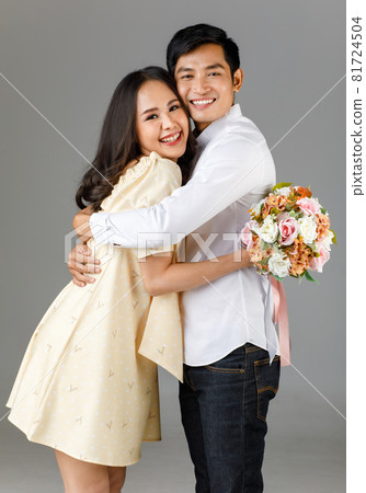 Portrait of young attractive Asian couple, man wearing white shirt, woman wearing beige dress hugging each other, woman holding bouquet of flower. Concept for pre wedding photography Portrait of young attractive Asian couple, man wearing white shirt, woman wearing beige dress hugging each other, woman holding bouquet of flower. Concept for pre wedding photography 81724504