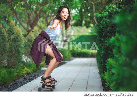 Asian young women surf skate or skates board outdoors on beautiful summer day. Happy young women play surf skate at park. 81725152