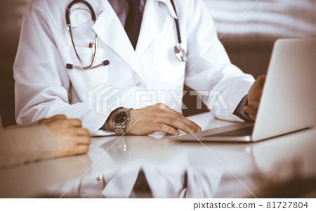 Unknown male doctor and patient woman discussing something while sitting in clinic and using laptop. Best medical service in hospital, medicine, pandemic stop Unknown male doctor and patient woman discussing something while sitting in clinic and using laptop. Best medical service in hospital, medicine, pandemic stop 81727804