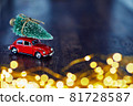 A festive New Year card with a space for text, sparkling lights, golden glitter, defocused lights and a red car on dark brown wooden background 81728587