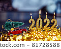 Festive New Year card with golden numbers of 2022, sparkling lights, golden glitter, defocused lights and a red car with a Christmas tree 81728588
