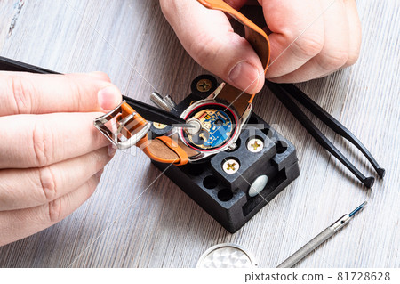 watch repairer workshop - watchmaker removes battery from quartz wristwatch with plastic tweezers on wooden table 81728628