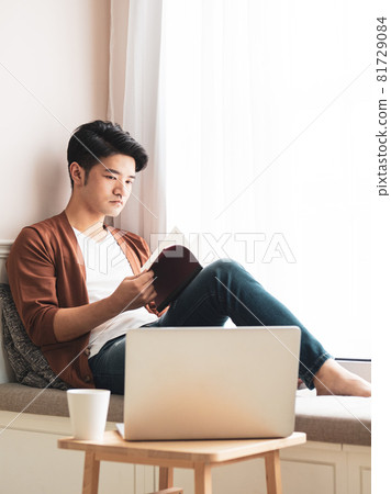 Young Asian man reading book while relaxing at home Young Asian man reading book while relaxing at home 81729084