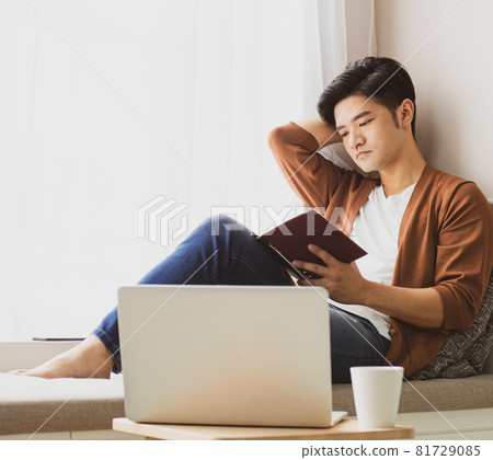 Young Asian man reading book while relaxing at home Young Asian man reading book while relaxing at home 81729085