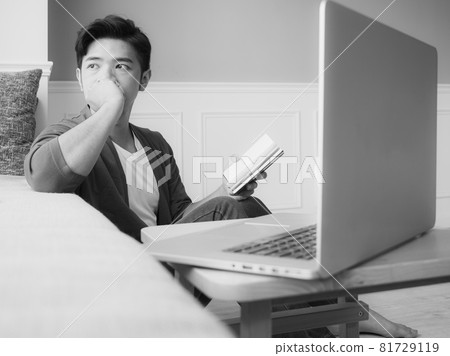 Young Asian man reading book while relaxing at home 81729119