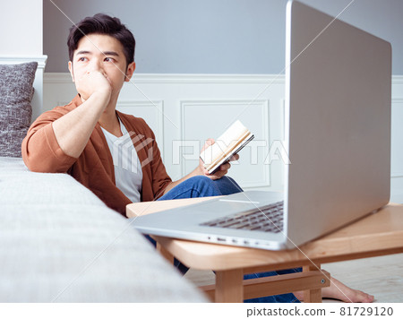 Young Asian man reading book while relaxing at home Young Asian man reading book while relaxing at home 81729120