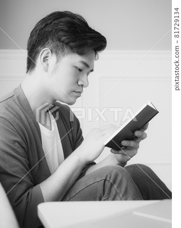 Young Asian man reading book while relaxing at home Young Asian man reading book while relaxing at home 81729134