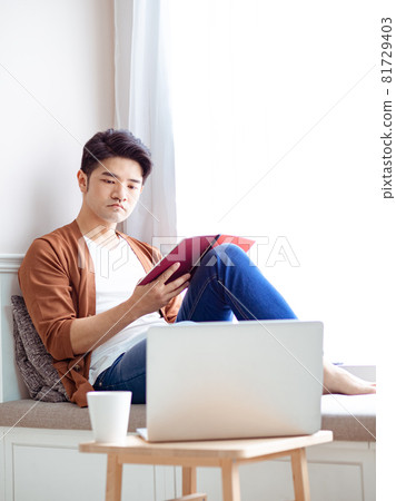 Young Asian man reading book while relaxing at home Young Asian man reading book while relaxing at home 81729403