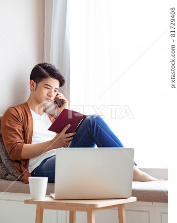 Young Asian man reading book while relaxing at home Young Asian man reading book while relaxing at home 81729408