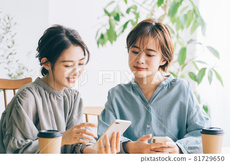 Two smiling women looking at a smartphone at a cafe Two smiling women looking at a smartphone at a cafe 81729650