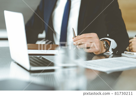 Unknown businessmen and woman sitting, using laptop computer and discussing questions at meeting in modern office, close-up Unknown businessmen and woman sitting, using laptop computer and discussing questions at meeting in modern office, close-up 81730211