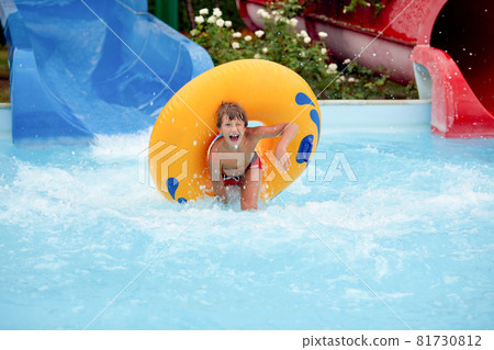 happy an 8 year old boy is riding in the water Park on inflatable circles on water slides with splash happy an 8 year old boy is riding in the water Park on inflatable circles on water slides with splash 81730812