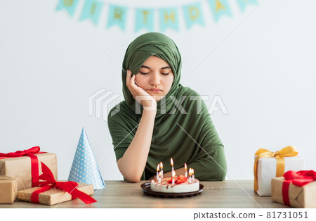Sad Indian teen girl in hijab having dull birthday party, feeling bored, celebrating holiday alone during covid Sad Indian teen girl in hijab having dull birthday party, feeling bored, celebrating holiday alone during covid 81731051