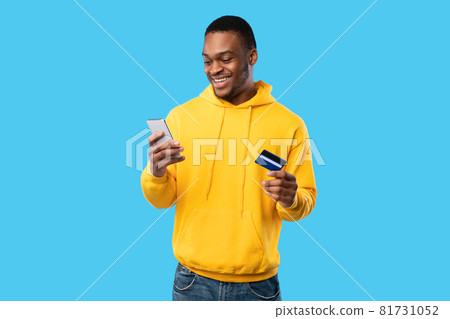 African American Man Using Credit Card And Cellphone, Blue Background African American Man Using Credit Card And Cellphone, Blue Background 81731052