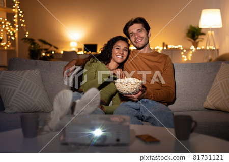 Happy Couple Watching Movie Using Home Cinema Projector Sitting Indoors 81731121