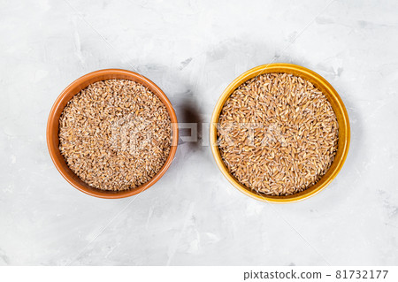 top view of crushed and whole Emmer farro hulled wheat grains in round ceramic bowls on gray concrete board 81732177