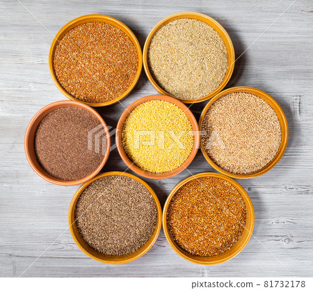 top view of various millet grains in round ceramic bowls on gray wooden table 81732178