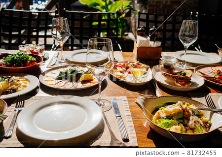 wooden table served with plates with salad and snacks, cutlery and glasses. wooden table served with plates with salad and snacks, cutlery and glasses. 81732455