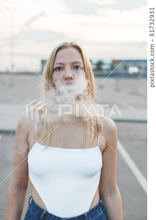 Blonde woman in city with electronic cigar vaping 81732931