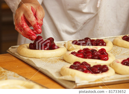Work in bakery, making fruit filled pies. The woman in the picture is making filled fruit pies. Hands filling pie yeast dough with strawberries. Work in the bakery. 81733652