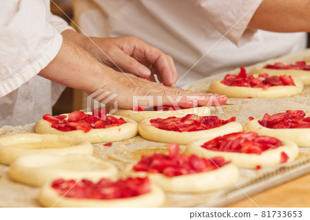 Work in bakery, making fruit filled pies. The woman in the picture is making filled fruit pies. Hands filling pie yeast dough with strawberries. Work in the bakery. 81733653