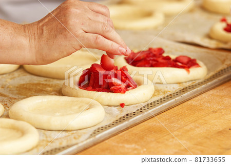 Work in bakery, making fruit filled pies. The woman in the picture is making filled fruit pies. Hands filling pie yeast dough with strawberries. Work in the bakery. 81733655