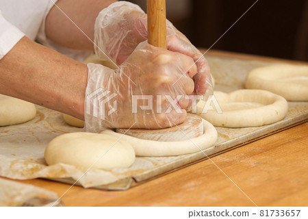 Work in bakery, making filled pies. The woman in the picture is making filled pies. Hands in protective gloves holding the tool press dough to get the proper shape of pie. Work in the bakery. 81733657