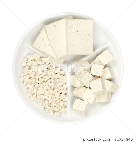 Processed white tofu, on a small white serving platter. Three slices, cubes and crumbled tofu. Bean curd made of coagulated soy milk, a component of Asian cuisine and meat substitute. Close-up. Photo. 81734840