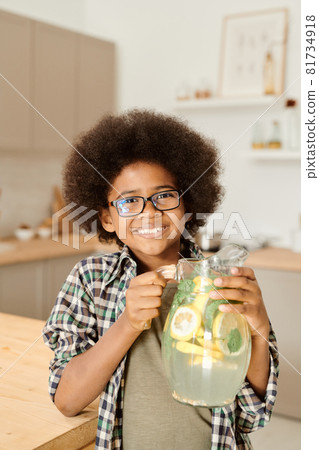 Smiling little boy of African ethnicity holding jug with fresh lemonade 81734918