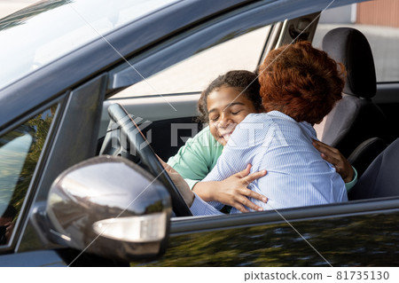 Happy schoolgirl embracing her mom while both sitting in the car Happy schoolgirl embracing her mom while both sitting in the car 81735130