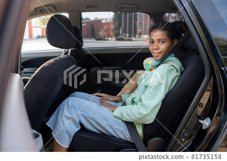 Happy youthful girl looking at you with smile from backseat of car Happy youthful girl looking at you with smile from backseat of car 81735158