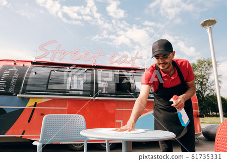 Young man in uniform spraying sanitizer on plastic table 81735331