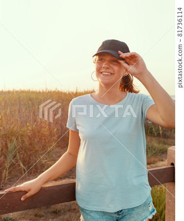 Smiling teenage girl in baseball cap standing near the field 81736114
