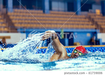 Professional male swimmer in swimming cap and goggles in motion and action during training at pool, indoors. Healthy lifestyle, power, energy, sports movement concept 81739006