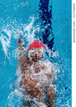 Top view of professional male swimmer in red swimming cap and goggles practicing and training at pool, indoors. Healthy lifestyle, power, energy, sports movement concept 81739008
