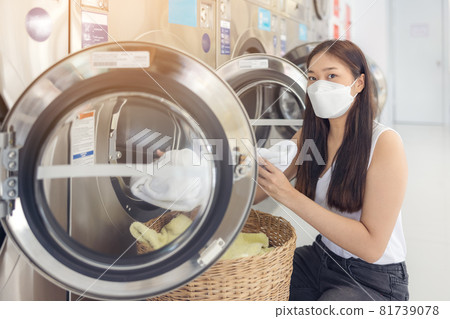 At a laundromat shop with many automatic washing machines, a beautiful woman wearing a mask is doing laundry. 81739078
