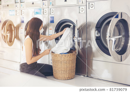 At a laundromat shop with many automatic washing machines, a beautiful woman wearing a mask is doing laundry. At a laundromat shop with many automatic washing machines, a beautiful woman wearing a mask is doing laundry. 81739079