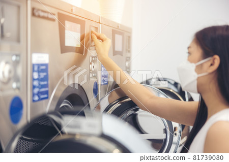 At a laundromat shop with many automatic washing machines, a beautiful woman wearing a mask is doing laundry. At a laundromat shop with many automatic washing machines, a beautiful woman wearing a mask is doing laundry. 81739080