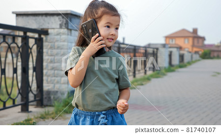 Little Korean girl talks on phone on empty city embankment Little Korean girl talks on phone on empty city embankment 81740107