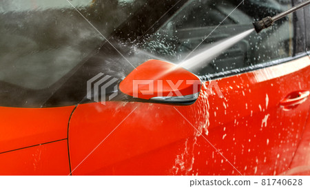 Side mirror of red car washed in self service carwash, jet water spraying from nozzle 81740628