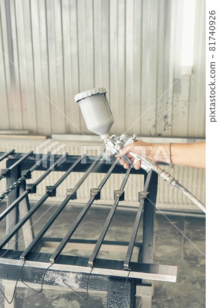 Woman paints forged balusters with spray gun in paint chamber 81740926