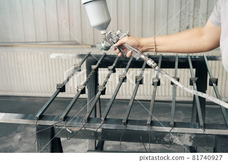 Woman paints forged balusters with spray gun in paint chamber 81740927